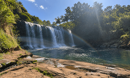 Waterfall cascading into a pool with sunlight and a rainbow.