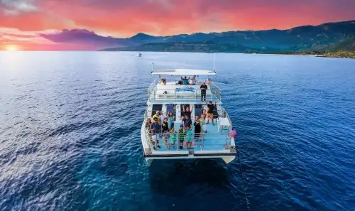 Boat with people on ocean at sunset, mountains in the distance.